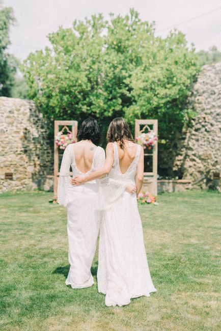 A floral arrangement featuring a variety of fresh flowers in soft pinks, whites, and greens, displayed in a wooden frame with two vertical supports placed on a grassy lawn. The arrangement includes ro