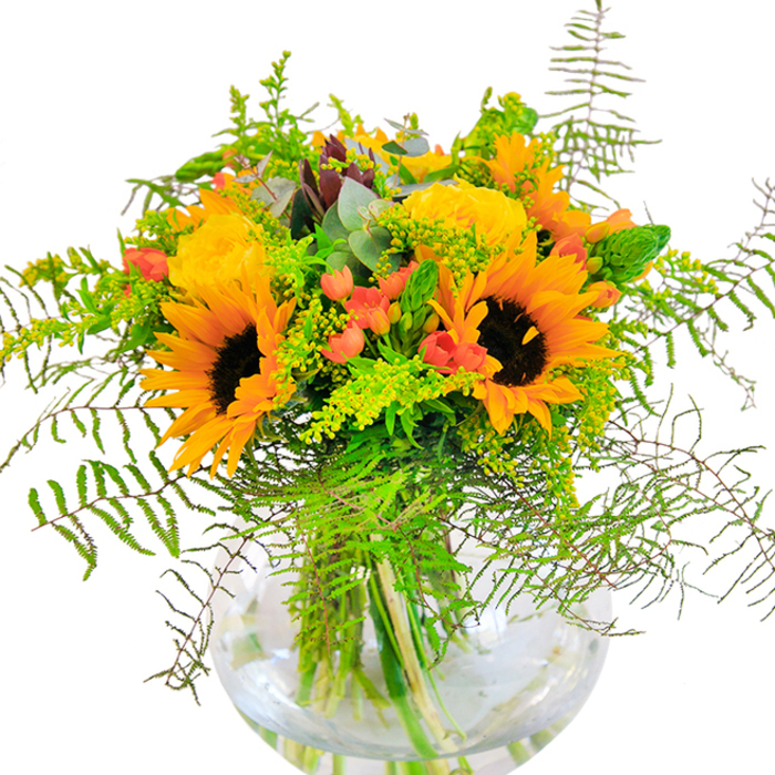 Upon first glance, this bouquet emanates a pure, sunlit exuberance that echoes the lively essence of West Green's bustling markets. Radiant sunflowers and golden roses beam side by side, petals unfurling in generous, overlapping layers that seem to capture the glow of a summer's afternoon near Philip Lane. Between these blossoms, deep green leaves and light, drifting vines cascade outward, creating movement and recalling the lush foliage found in gardens across the N15 area. Glossy red hypericum berries sparkle among the greenery, their vivid skins contrasting beautifully with the matte texture of the rose and sunflower petals. The arrangement is gathered in a smooth, fishbowl-like glass vase, its transparency revealing the refreshing tangle of stems and water-a testament to both freshness and careful design. On closer inspection, the tactile contrasts reveal themselves: suede-soft sunflower petals, tightly packed rose whorls, and the cool crispness of fern and eucalyptus. The bouquet emits a delicate, lively scent, evoking fresh air and sun-drenched fields, making it a perfect choice for joyful milestones. Whether marking a birthday, an anniversary, or simply bringing cheer to a neighbour's doorstep, this arrangement channels happiness straight from West Green's floral heart.