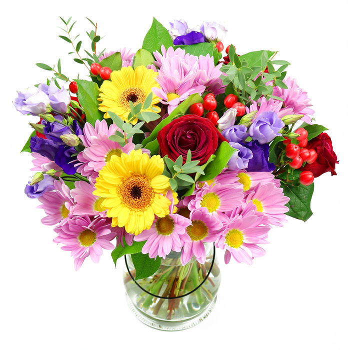 This image shows a full, exuberant bouquet arranged in a clear cylindrical glass vase, positioned against a bright white background that lets every stem and petal stand out with clarity. At the centre, rich red roses unfurl their velvety petals in tight spirals, giving the design a core of classic elegance that feels at home in both modern flats and traditional houses around West Green. Just off-centre, yellow gerbera daisies with dark, textured centres beam out in bold circles, their smooth petals radiating warmth and optimism, like sunshine breaking through over nearby Downhills Park. Encircling these feature blooms are plentiful pink and lavender daisies or chrysanthemums, each flower composed of many slim, soft petals and tiny yellow centres, creating a cushion of pastel colour that adds width and softness to the composition. Interlaced among the daisies are graceful lisianthus stems, their bell-shaped flowers in shades of purple and lilac lending cool tones and gentle curves, a pleasing contrast to the structured discs of the gerberas. Bright red hypericum berries are tucked between leaves and petals, rounding out the design with playful, berry-like clusters that catch the light. The bouquet is wrapped in generous foliage, from bold, dark green leaves that frame the arrangement to finer, lighter green sprigs that give a sense of movement and airy freshness, reminiscent of greenery lining the quieter residential streets off West Green Road. Through the transparent vase, you can see the carefully trimmed stems arranged neatly in clear water, evidence of professional care and conditioning. The whole arrangement feels joyful yet refined, ideal as a thoughtful gift for birthdays, congratulations, or to lift the mood of a living room or office in the West Green area with a burst of natural colour and life.